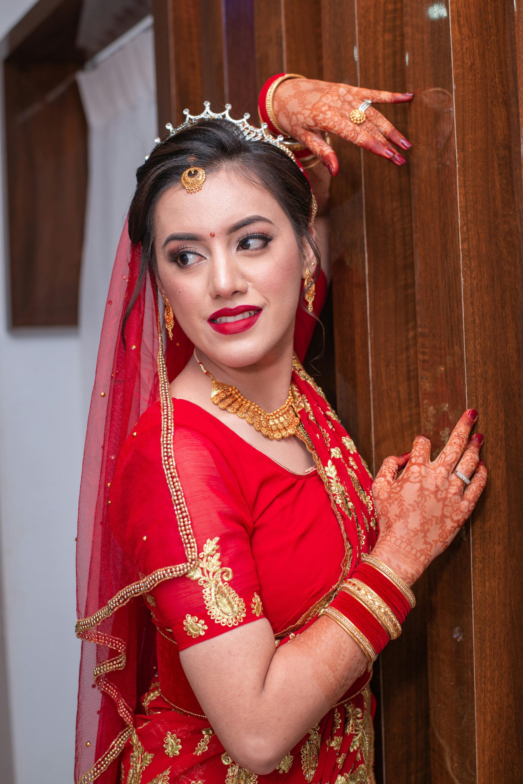 Stunning Nepali bride in vibrant red attire with intricate henna design and traditional jewelry.